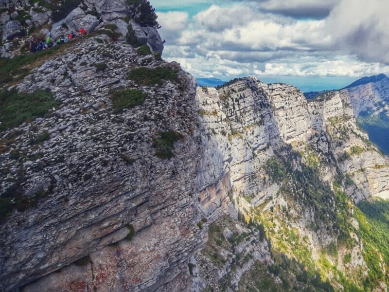 Sentier de montagne escarpé avec des coureurs de trail progressant le long d'une crête rocheuse sous un ciel nuageux