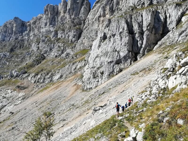 Groupe de coureurs de trail descendant un sentier de montagne caillouteux au pied de falaises abruptes