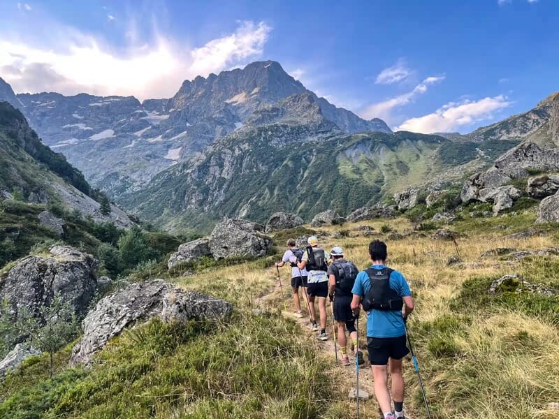 Un groupe de coureurs en trail marche sur un sentier de montagne entouré de rochers et de végétation.