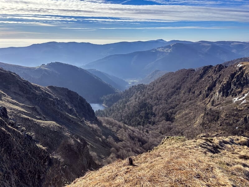 Paysage montagneux avec une vallée profonde et boisée sous un ciel partiellement nuageux au Col de la Schlucht.