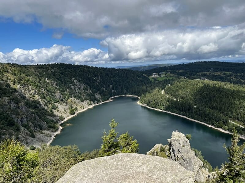 Vue aérienne d'un lac en forme de cœur entouré de forêts denses sous un ciel nuageux.