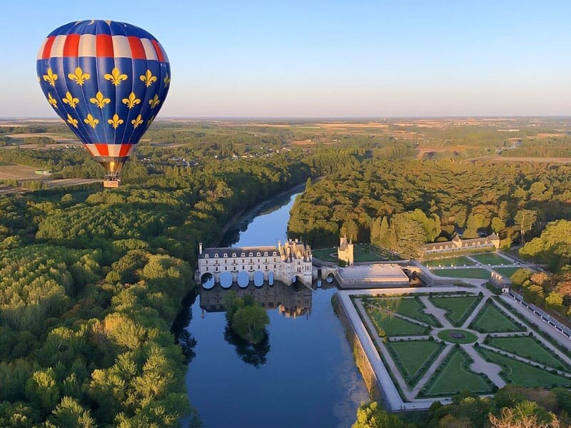 Vue aérienne d'une montgolfière colorée flottant au-dessus du Château de Chenonceau et ses jardins à la française, entouré de forêts et de champs