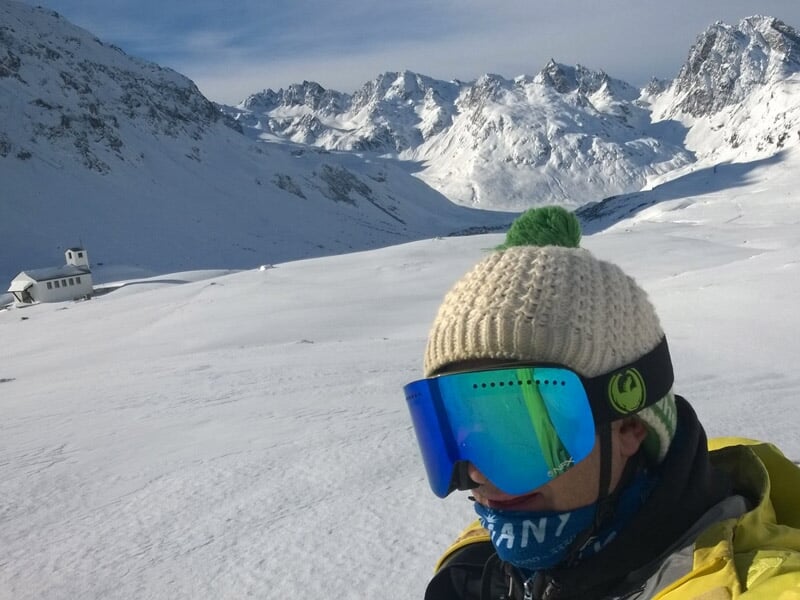 Personne en bonnet et lunettes de ski prenant un selfie avec un paysage de montagne enneigée en arrière-plan.