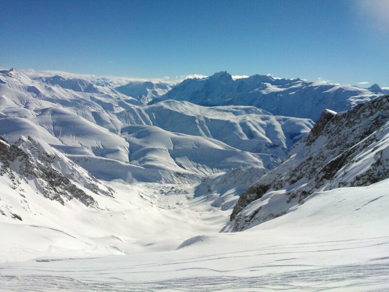 Vue panoramique d'une vallée et montagnes enneigées sous un ciel bleu clair sans nuages.