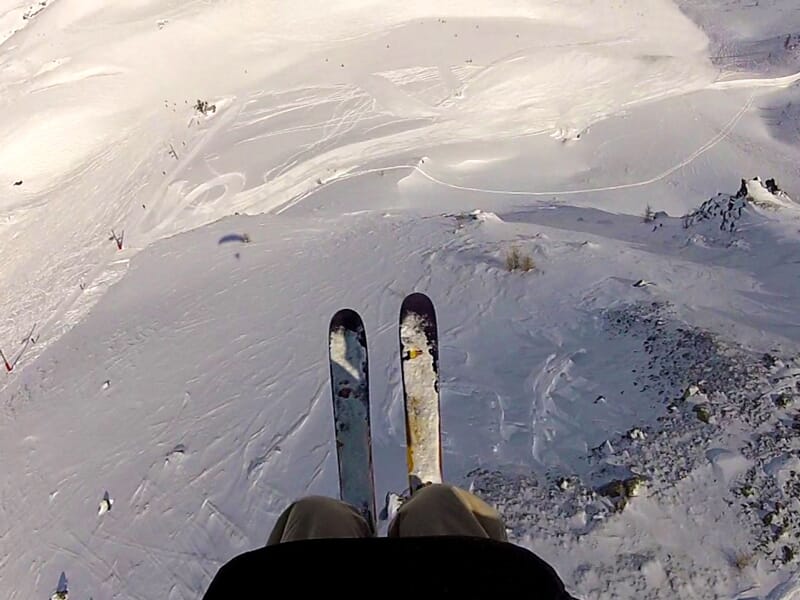 Vue en plongée sur des skis en action lors d'une descente en ski parapente sur une pente enneigée en montagne.