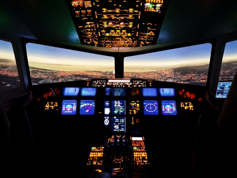 Cockpit d'un simulateur de pilotage d'avion avec vue panoramique sur un paysage urbain au crépuscule.