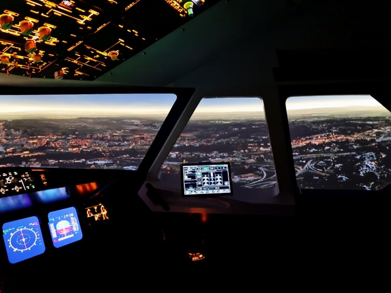 Intérieur d'un simulateur d'avion montrant les instruments de vol et un écran avec paysage urbain.