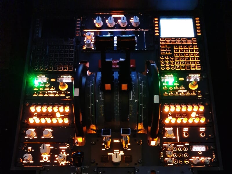 Panneau de commandes d'un simulateur d'avion avec multiples boutons et leviers éclairés en orange.