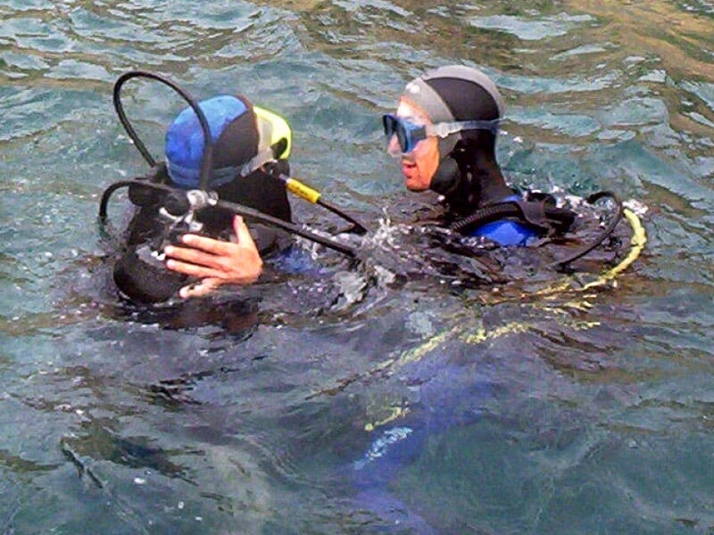 Un instructeur de plongée en combinaison noire aide un plongeur débutant dans l'eau calme.