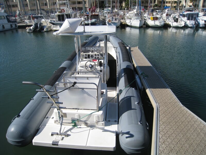 Bateau pneumatique gris amarré dans un port, prêt pour une sortie en mer avec équipements visibles.