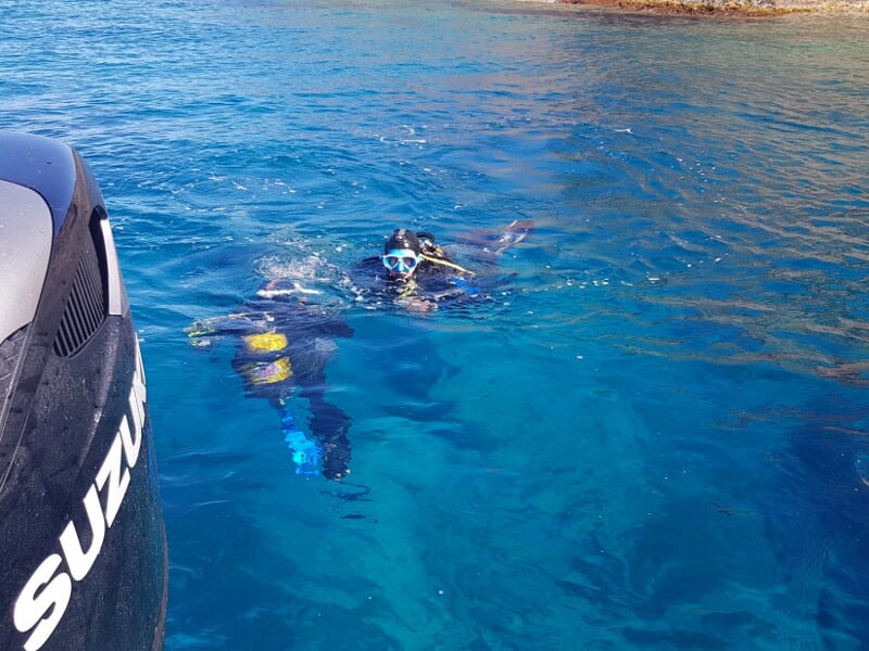 Deux plongeurs en surface près d'un bateau avec moteur Suzuki, dans une eau turquoise claire et calme.