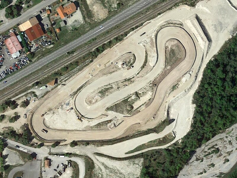 Vue aérienne d'un circuit de rallye terre avec plusieurs virages serrés et zones dégagées.