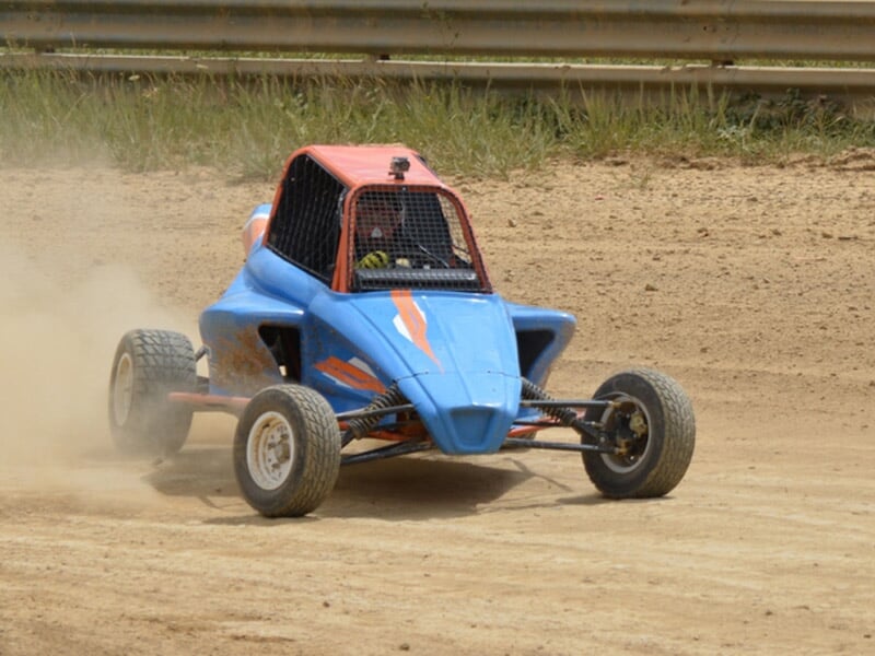 Buggy bleu sur piste terre, en virage serré avec poussière soulevée, pilote casqué visible.