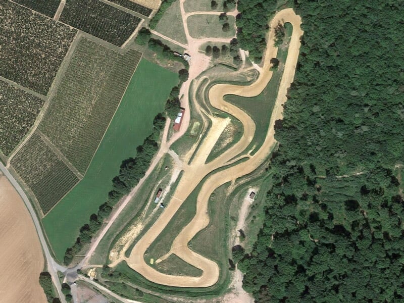 Vue aérienne d'un circuit de rallye terre entouré de forêt et de champs, piste sinueuse.
