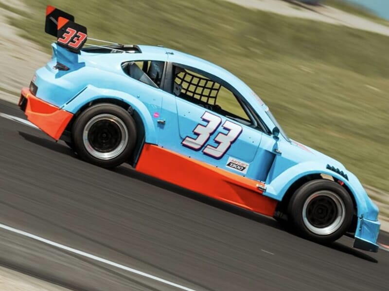 Voiture mitjet bleu ciel et orange lancée sur un circuit.