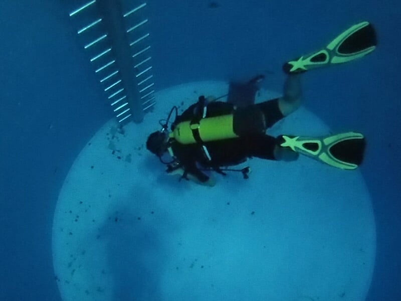 Plongeur équipé de palmes jaunes et bouteille d'air, explorant un grand puits d'eau profonde sous-marine.