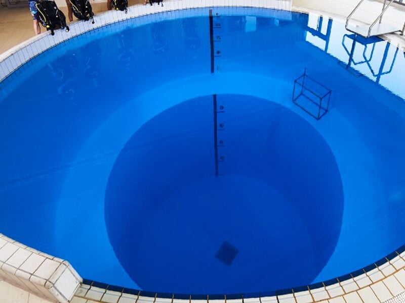 Piscine circulaire avec un grand puits d'eau profonde au centre, entourée de margelles blanches.