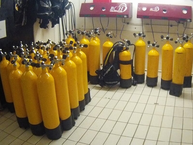 Rangée de bouteilles de plongée jaunes alignées sur un sol carrelé dans une salle d'équipement.