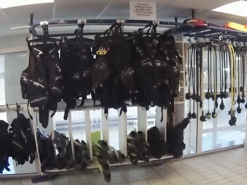 Équipement de plongée suspendu, comprenant gilets stabilisateurs et détendeurs, dans une salle claire.