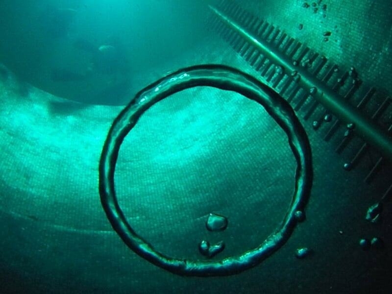 Anneau de bulles d'air sous l'eau dans un puits profond, avec une échelle métallique visible en arrière-plan.