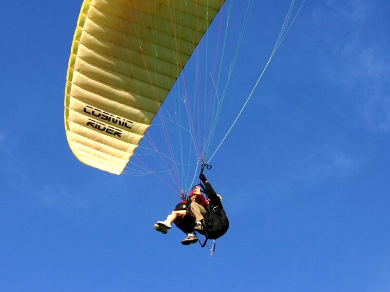 Parapentiste en plein vol sous une voile jaune avec l'inscription 