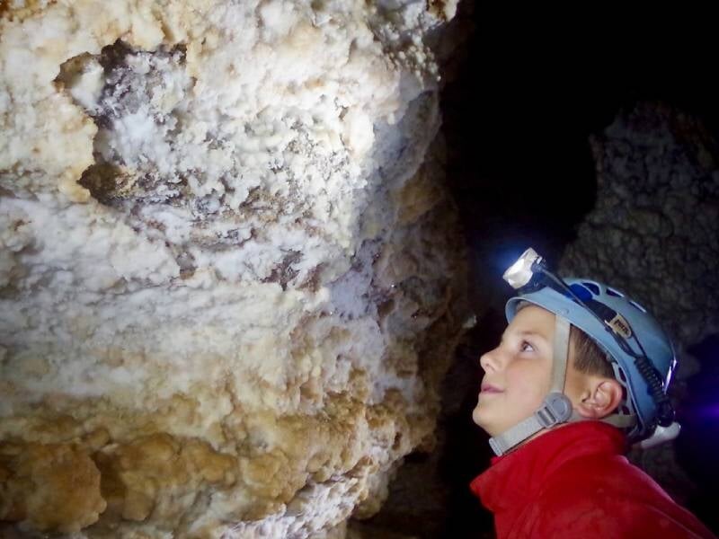 Enfant observant de près une paroi rocheuse dans une grotte, portant un casque de spéléologue avec lampe frontale allumée.