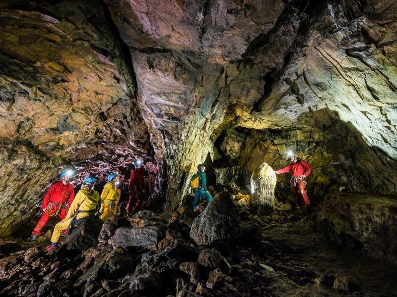 Groupe de spéléologues explorant une caverne, illuminée par leurs lampes frontales, avec des formations rocheuses impressionnantes.