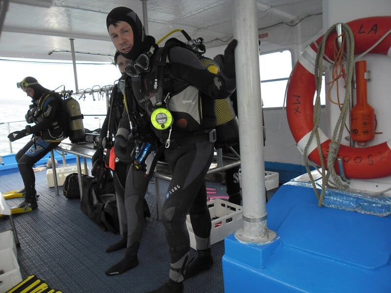 Deux plongeurs en combinaison noire se préparent à plonger depuis un bateau avec équipement complet.