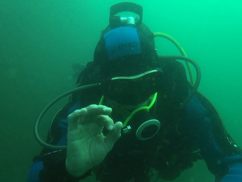 Plongeur en combinaison complète sous l'eau à Dinard, faisant le signe OK avec la main pendant un baptême de plongée.