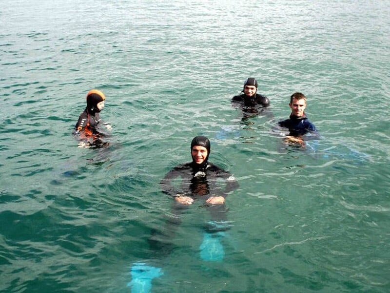Quatre plongeurs en combinaison noire avec palmes bleues dans une eau calme, prêts pour un baptême de plongée à Quiberon.