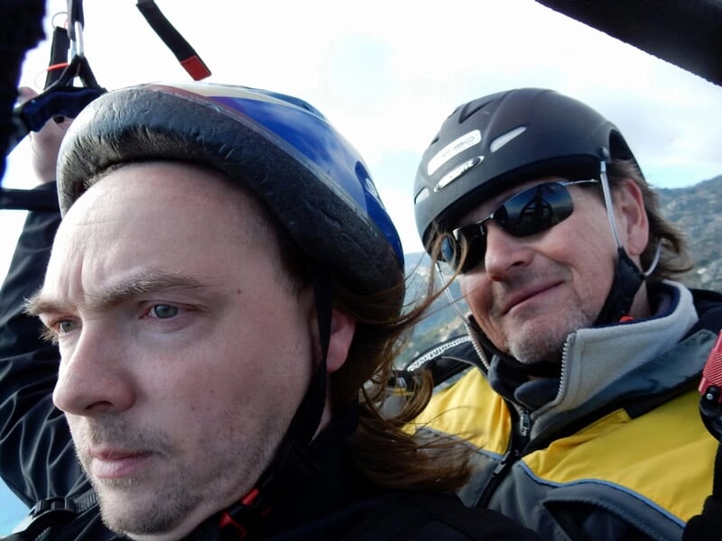 Gros plan sur deux hommes en vol en paramoteur, portant casque et lunettes de soleil.