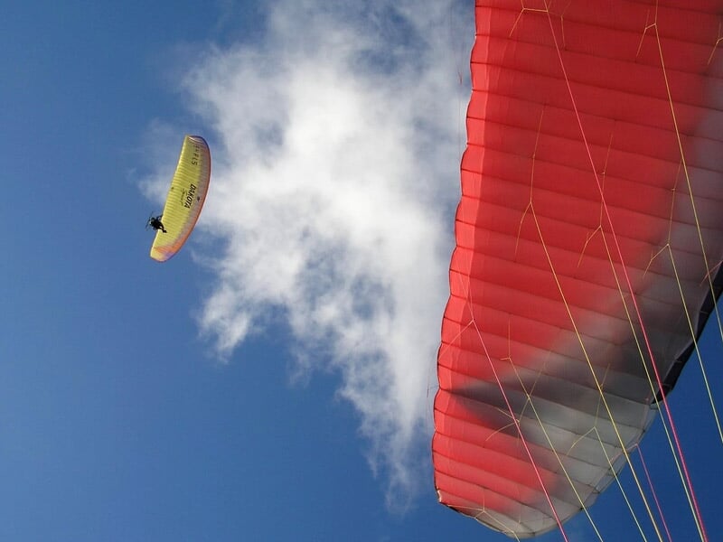 Paramoteur jaune volant sous un ciel bleu avec quelques nuages blancs.