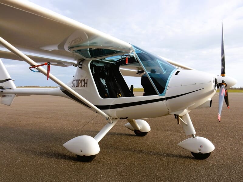Avion ULM blanc avec cockpit ouvert sur l'aérodrome de Nancy Essey sous un ciel partiellement nuageux.