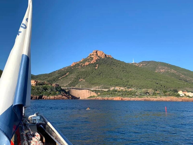 Vue depuis un bateau sur une mer calme avec une montagne verte et un ciel bleu clair en arrière-plan.