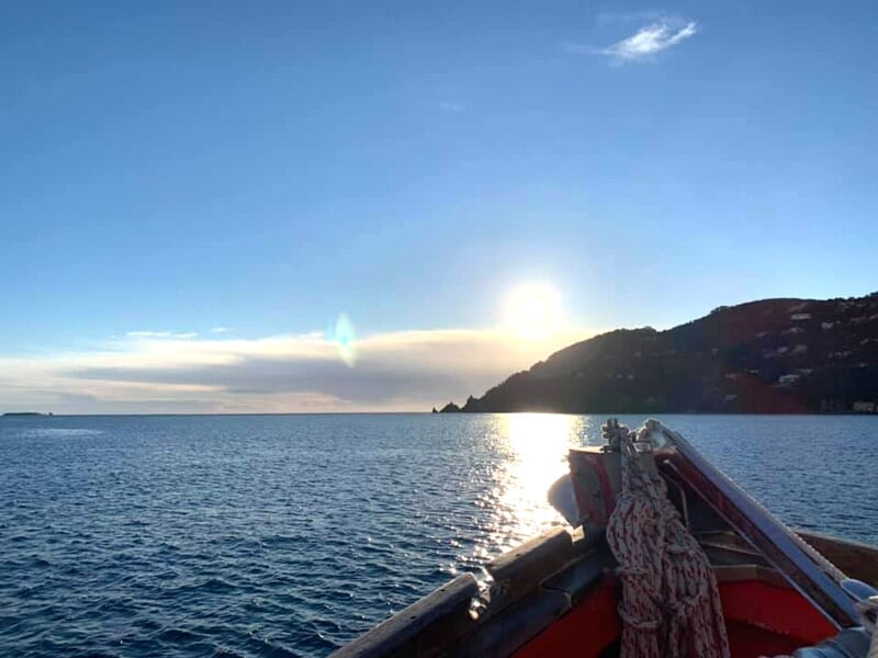 Soleil bas sur l'horizon illuminant la mer calme avec la proue d'un bateau visible au premier plan.