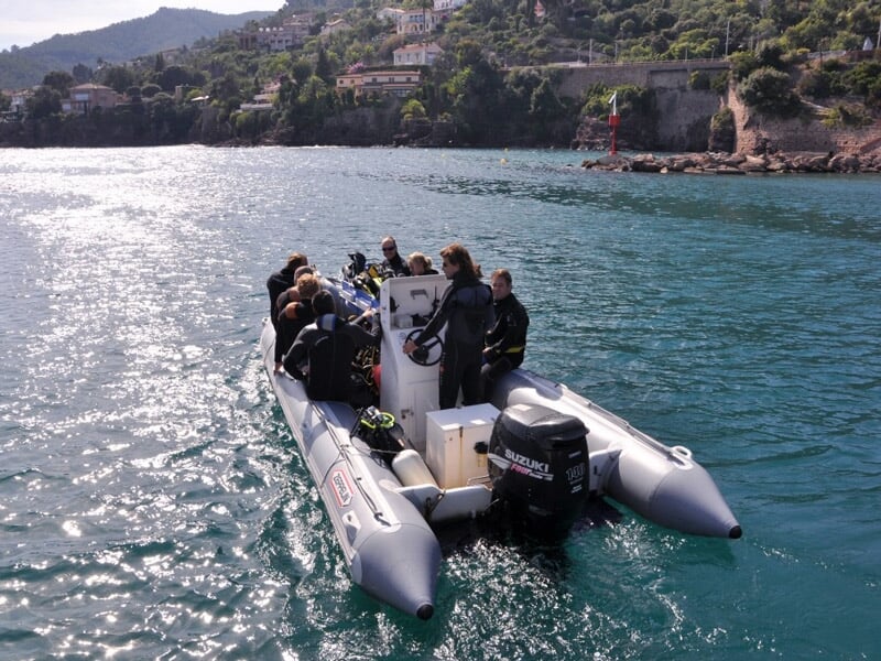 Groupe de personnes en combinaison de plongée sur un bateau pneumatique en mer calme.