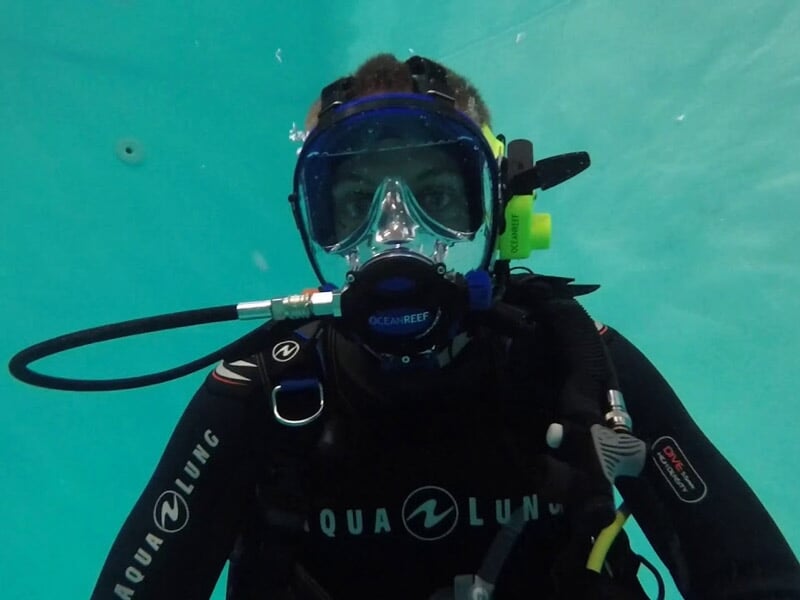 Plongeur équipé d'un masque et détendeur sous l'eau, prêt pour une séance de baptême de plongée en piscine.