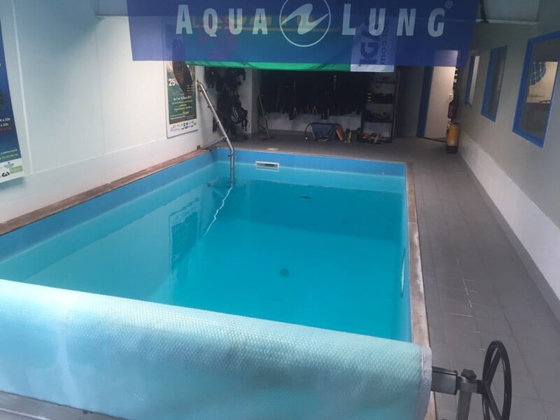 Piscine intérieure avec eau claire, équipée pour des baptêmes de plongée, avec une bannière Aqua Lung visible.