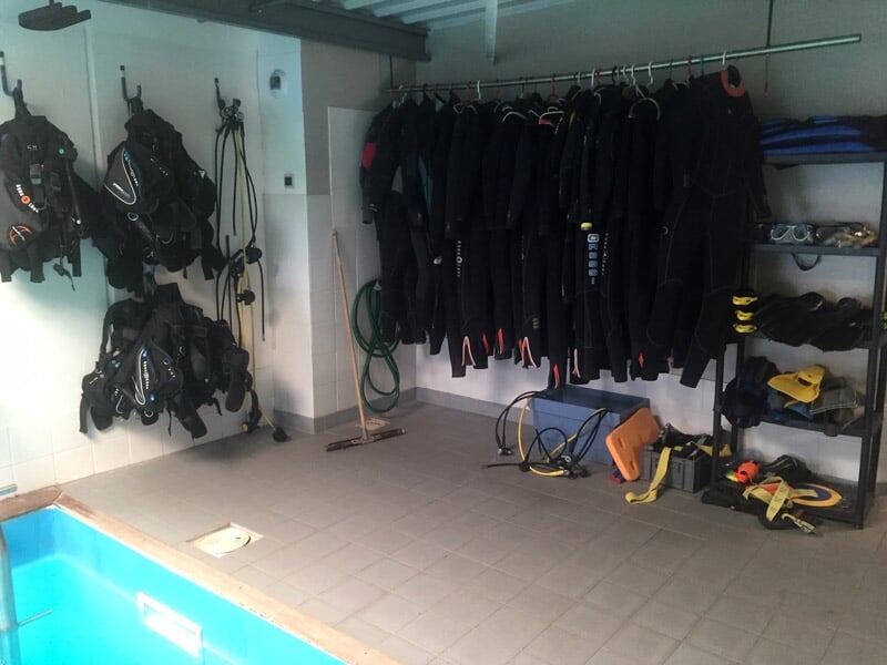 Salle de plongée avec combinaisons et équipements suspendus, prête pour une initiation à la plongée sous-marine.