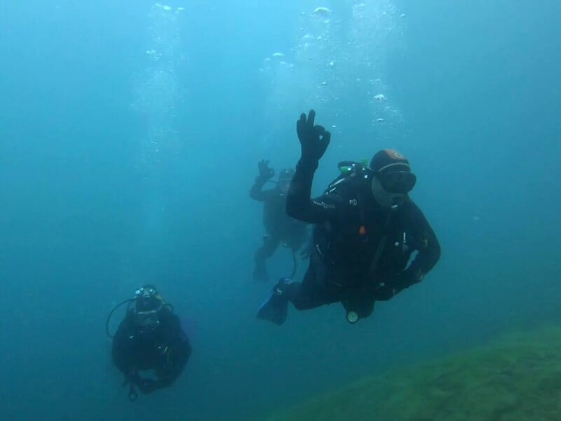 Groupe de plongeurs sous l'eau, l'un d'eux fait un signe de la main pour indiquer que tout va bien.