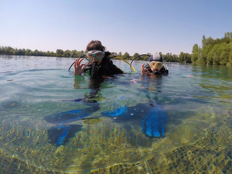 Deux plongeurs en surface dans un plan d'eau naturel, équipés de masques et tubas, profitant d'une initiation à la plongée.