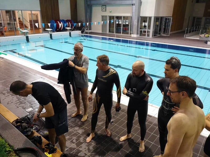 Groupe d'hommes en combinaison de plongée au bord d'une piscine, préparant leur matériel pour un stage d'initiation.