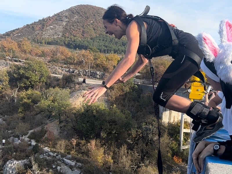 Personne en tenue de saut élastique en train de sauter depuis un pont, avec un paysage naturel en arrière-plan.