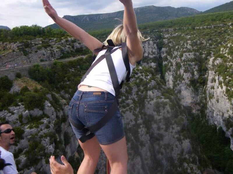 Femme en short et harnais prête à sauter à l'élastique depuis un pont au-dessus d'un canyon rocheux.