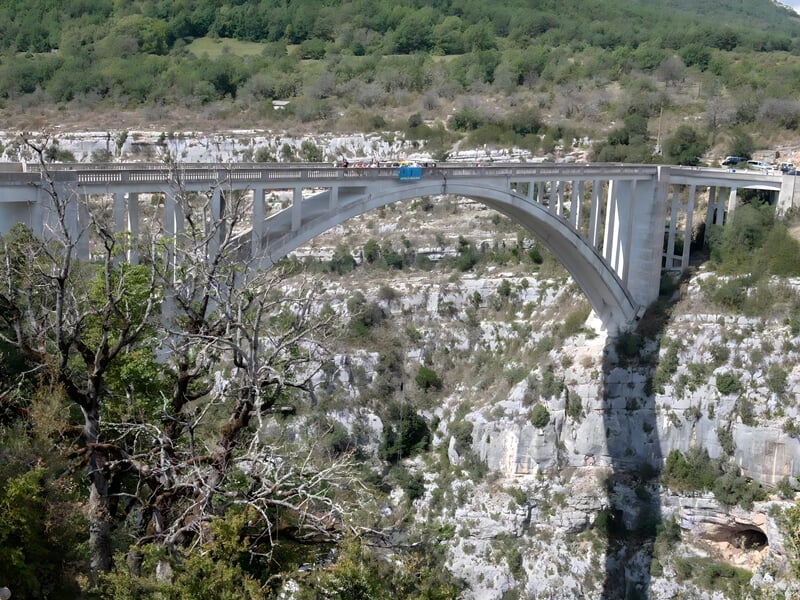 Vue panoramique d'un pont en arc surplombant un canyon avec une route et des voitures dessus.