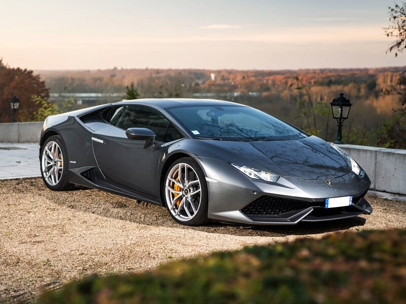 Voiture de sport grise stationnée sur une allée avec un paysage automnal en arrière-plan.