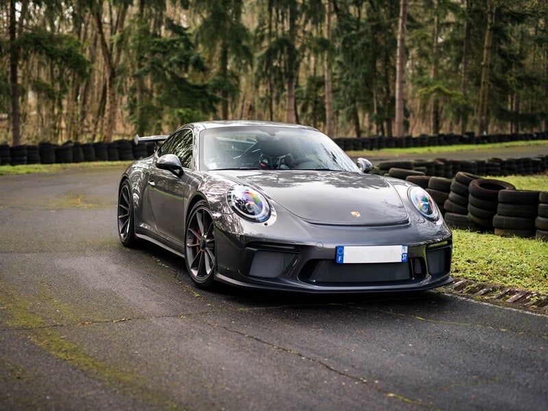 Voiture de sport grise foncée roulant sur une piste entourée d'arbres et de pneus de sécurité.