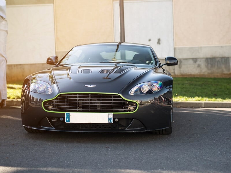 Voiture noire vue de face garée devant un mur clair avec des fenêtres et un sol en pavés.