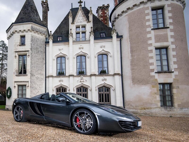 Voiture décapotable noire garée devant un château blanc avec des tours et un ciel clair.