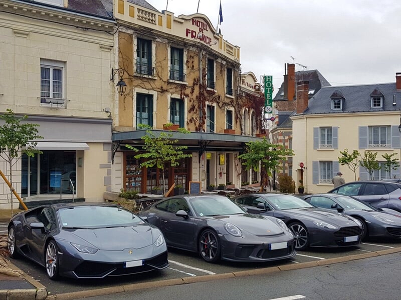 Trois voitures de sport garées devant un bâtiment ancien dans une petite ville avec des maisons.